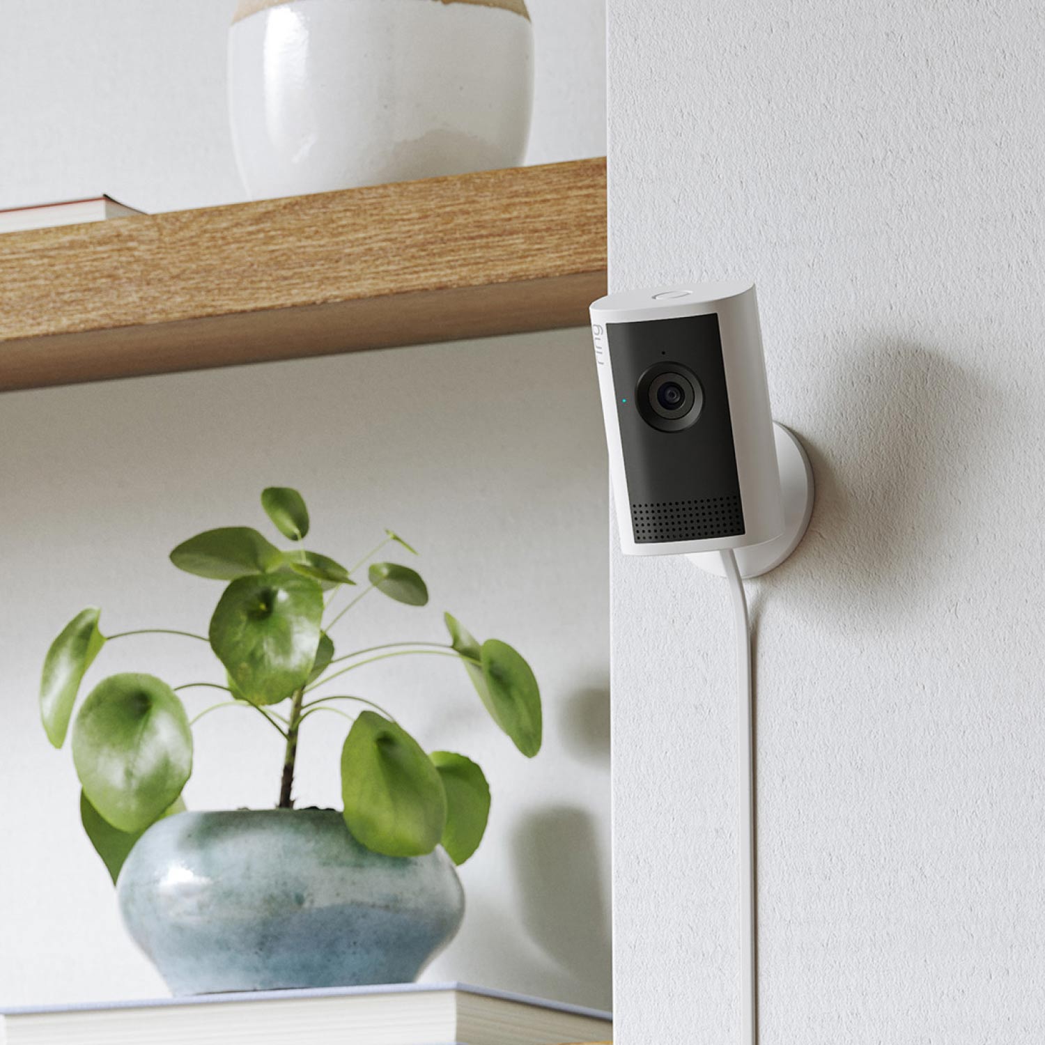 Indoor Cam Plus (Featuring Retinal 2K) - A white Indoor Cam Plus positioned on a shelf alongside a spray bottle and wire storage basket.