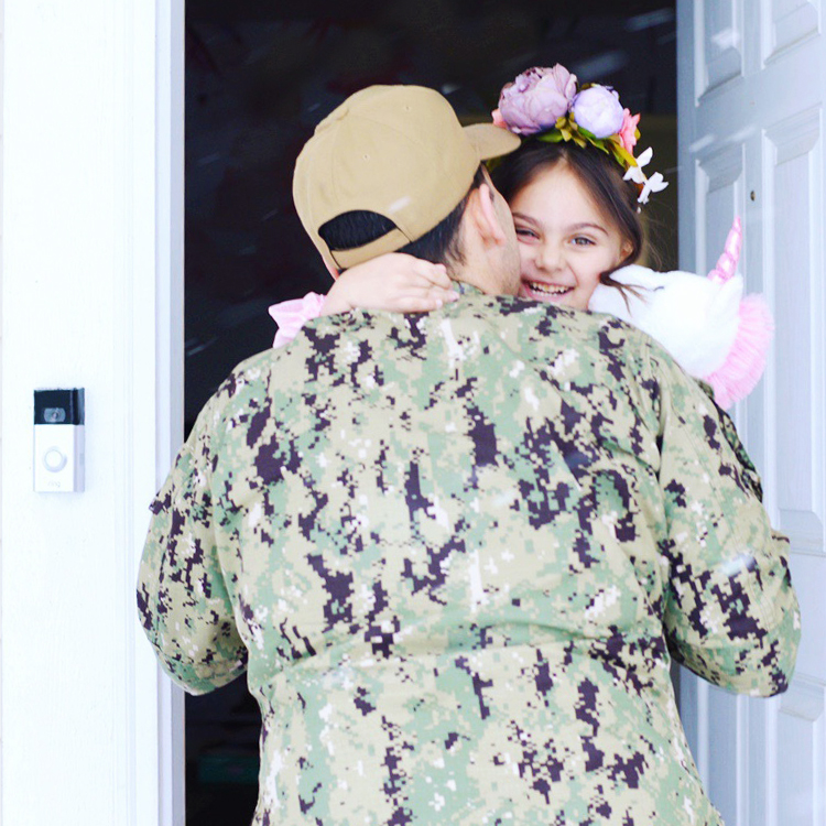 Military service member hugs smiling child at open front door with a Ring doorbell installed on the wall.