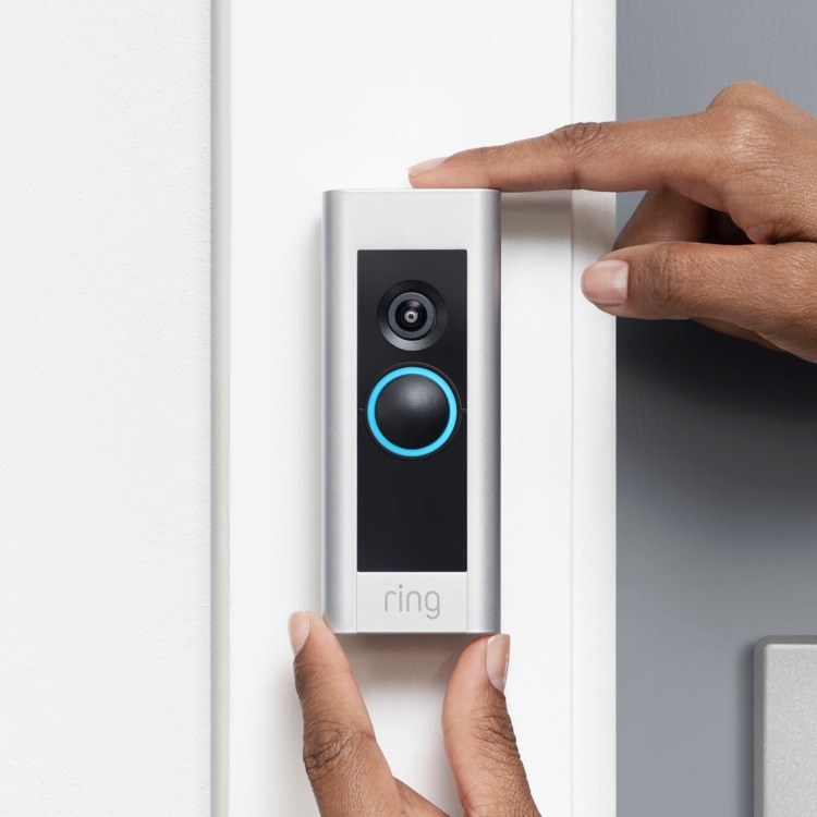 Person installing a Ring Video Doorbell on a white doorframe next to a grey door.