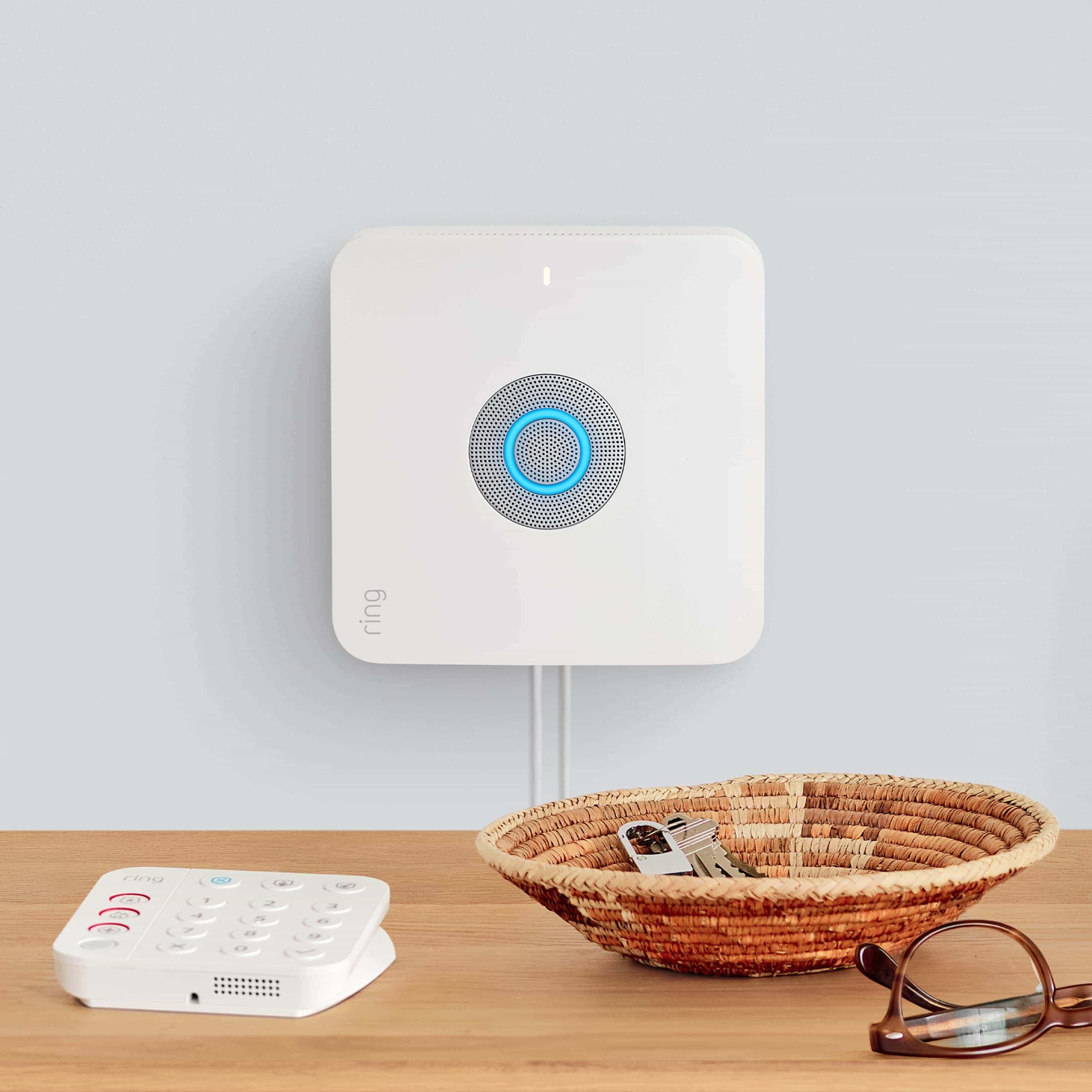 Alarm Security Kit, 8-Piece (2nd Generation) - wall-mounted Ring Alarm Base Station with glowing blue, by tabletop Ring Alarm Keypad, a basket of keys, and glasses.