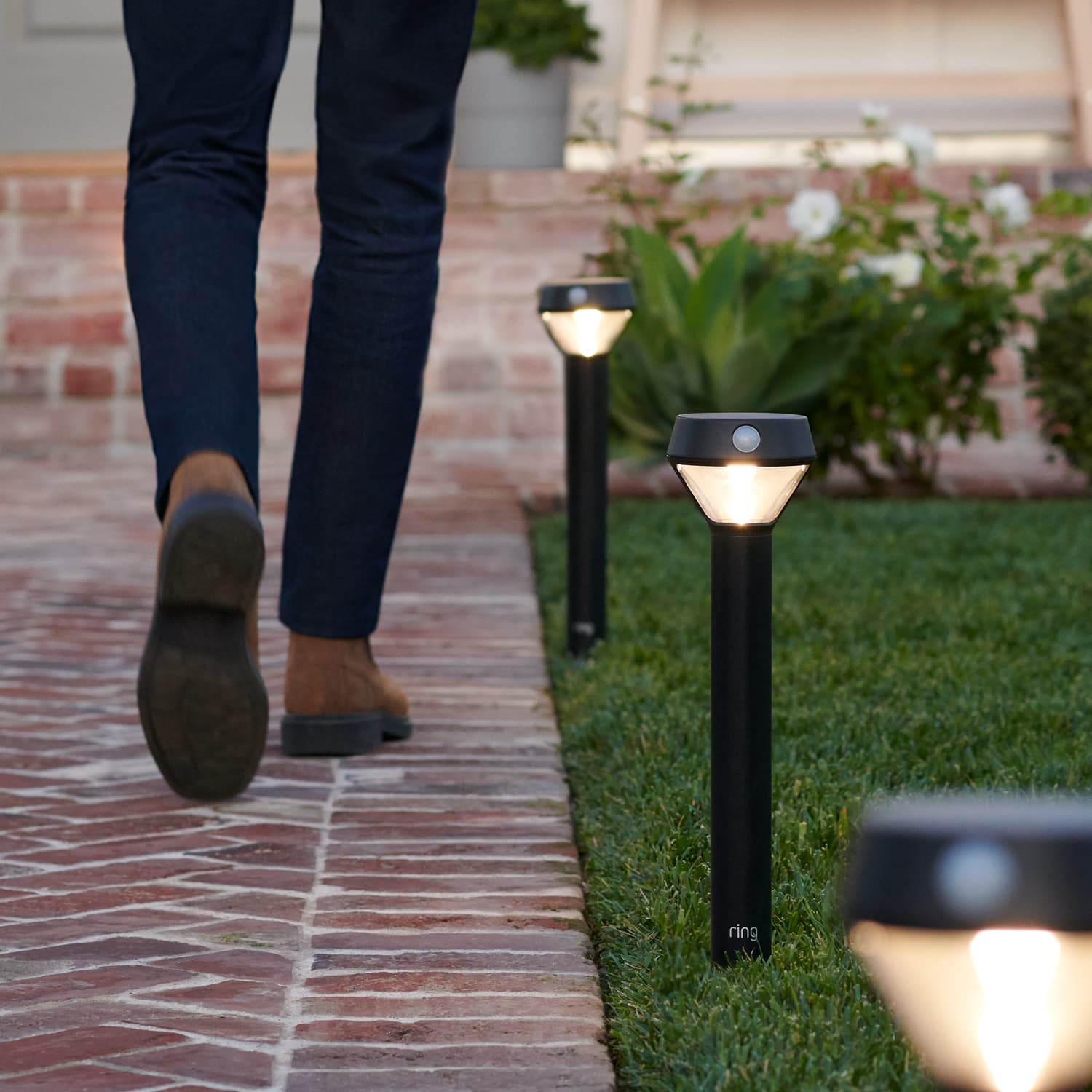 Smart Lighting Solar Pathlight - Person walking along a brick path, illuminated by motion-activated Ring Solar Pathlights.