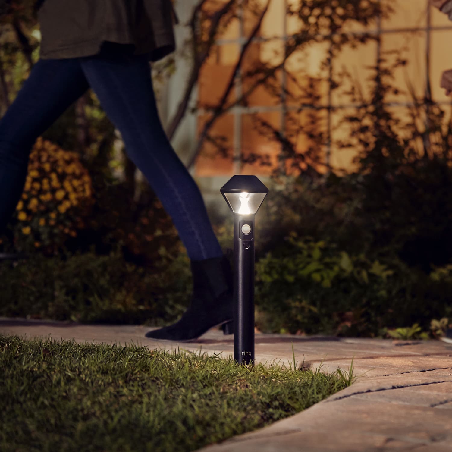 Smart Lighting Solar Pathlight - Person walking on a path past a Ring Solar Pathlight that automatically turns on when motion is detected.