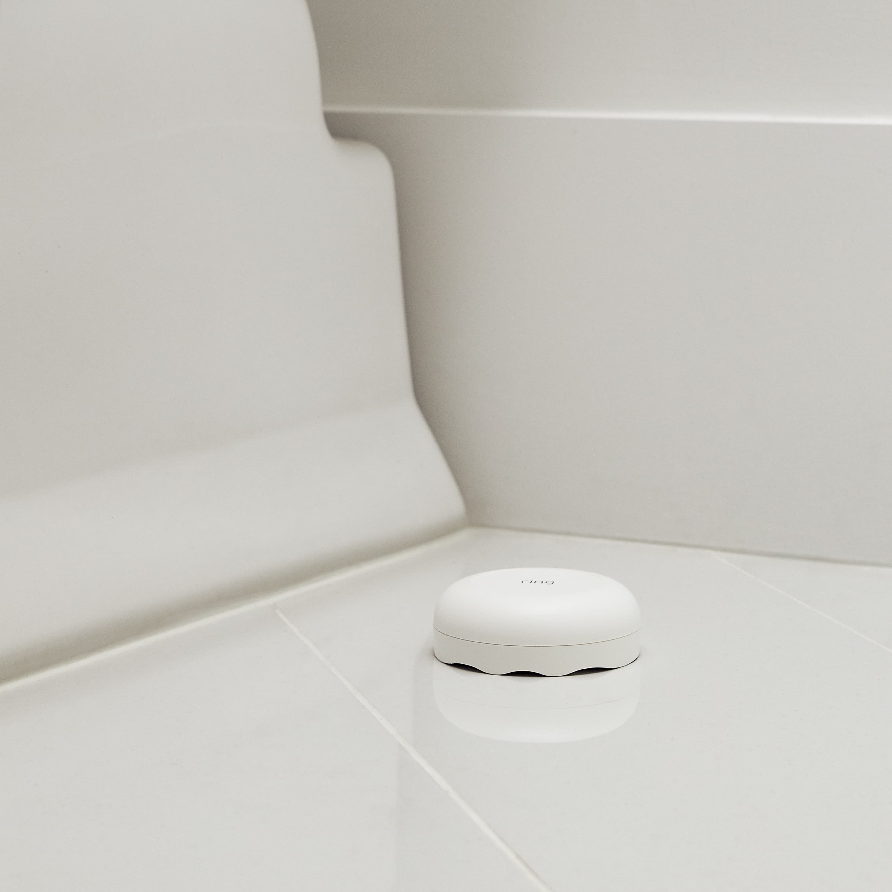 Flood & Freeze Alarm Bundle - White Ring Alarm Flood and Freeze Sensor placed on the tiled bathroom floor near a bathtub. 