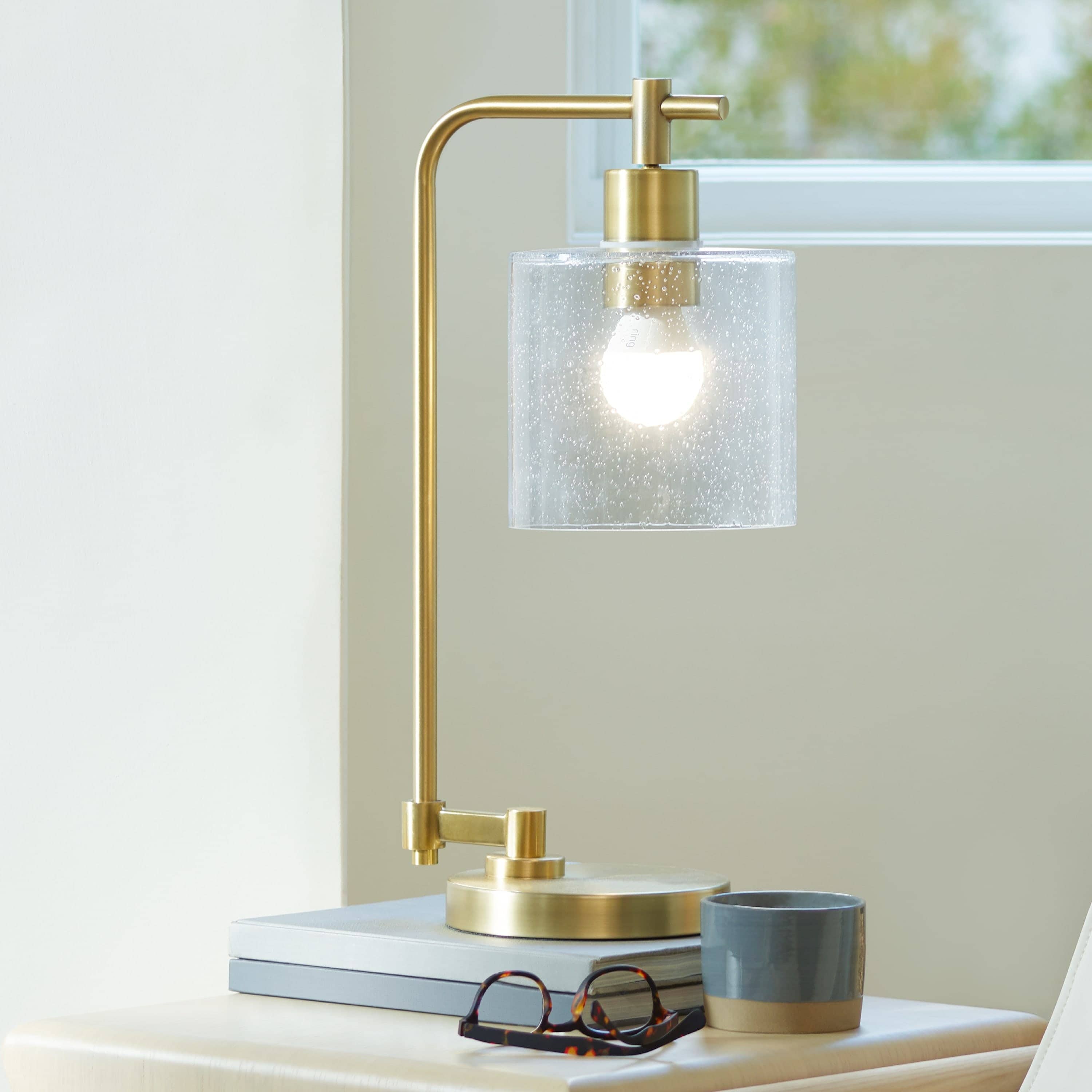 Smart Lighting A19 Smart LED Bulb - A19 Smart LED Bulb glowing inside a modern gold desk lamp with clear glass shade, on a nightstand.