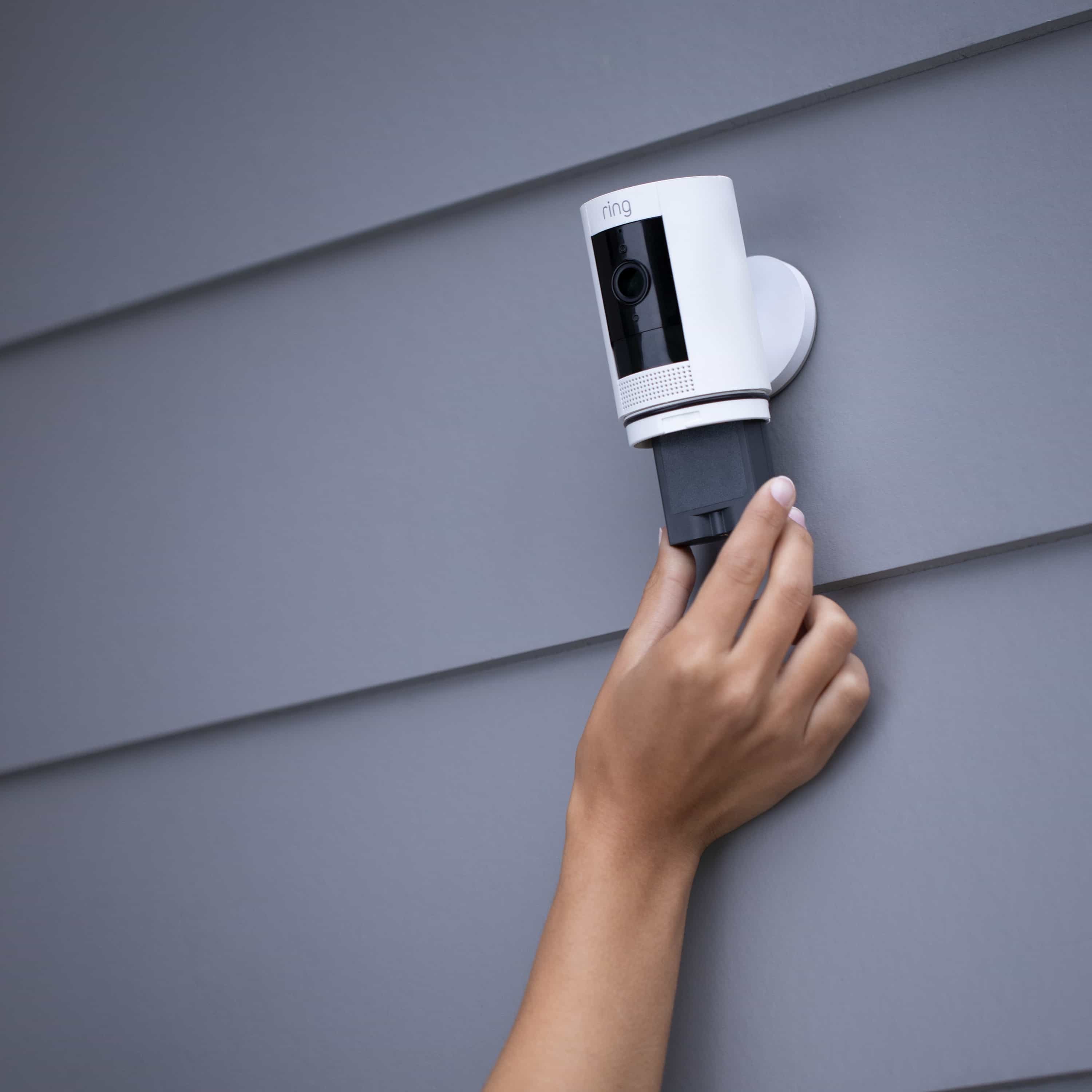 Charging Station + 2 Quick Release Battery Packs - Person removing a Ring Quick Release Battery Pack from a mounted Ring Stick Up Cam on grey siding.