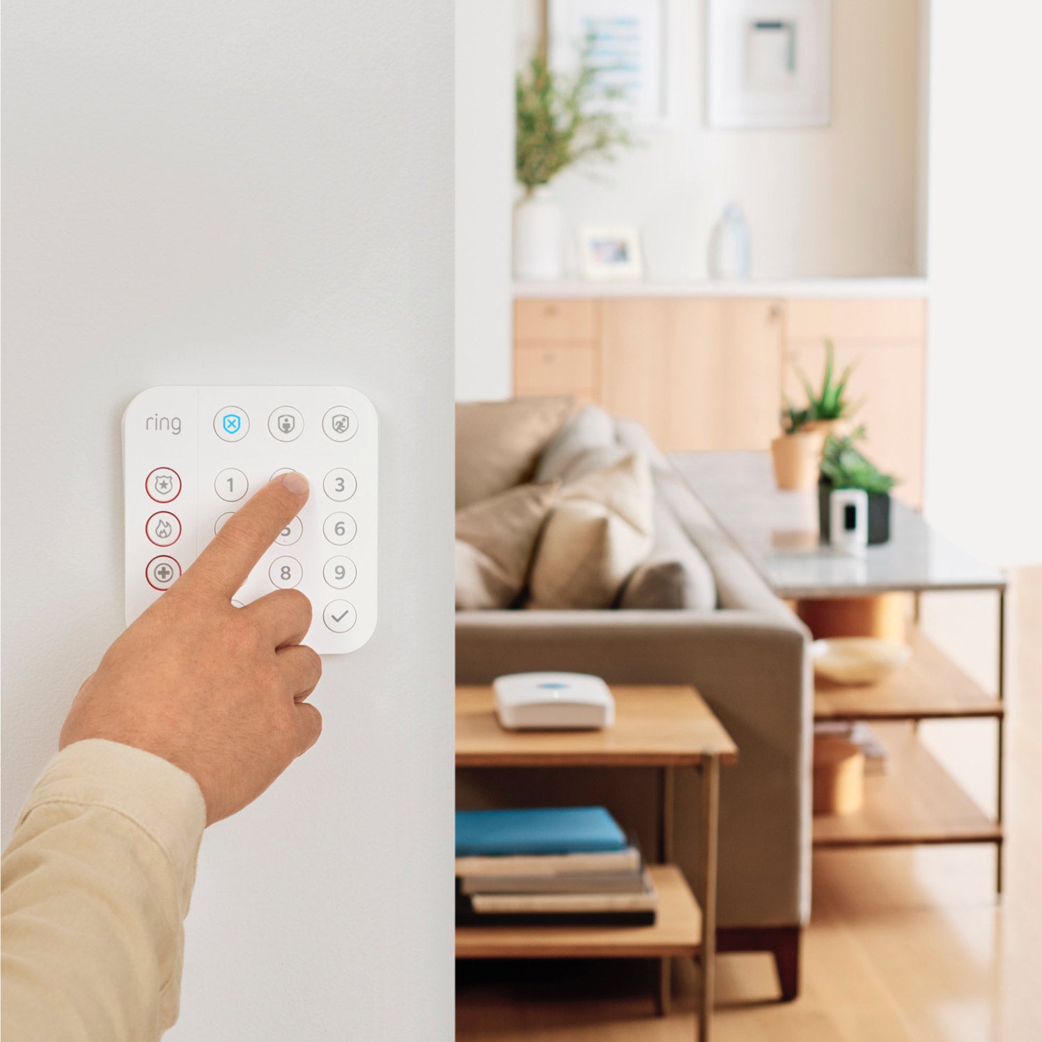 Alarm Pro Security Kit, 8-Piece (with built-in eero Wi-Fi 6 router) - Person pressing button on Ring Alarm Keypad mounted on wall, with a living room and Ring Alarm Pro Base Station visible.