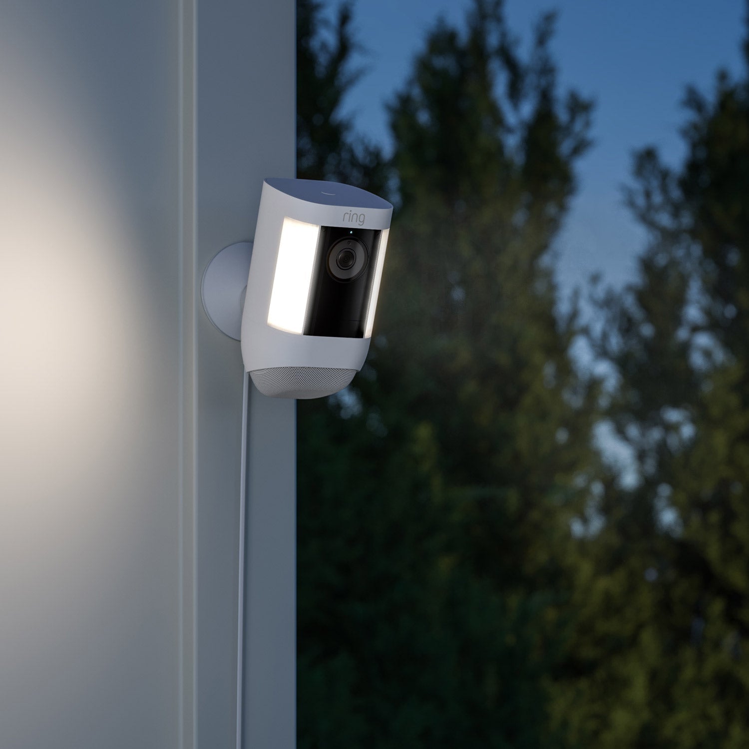 Indoor/Outdoor Power Adapter (USB-C) (for Outdoor Cam Plus, Outdoor Cam Pro, Stick Up Cam Pro, Spotlight Cam Plus, Spotlight Cam Pro)  - White Ring Spotlight Cam Pro with illuminated lights, mounted on a wall and powered by a USB-C cable, at dusk.