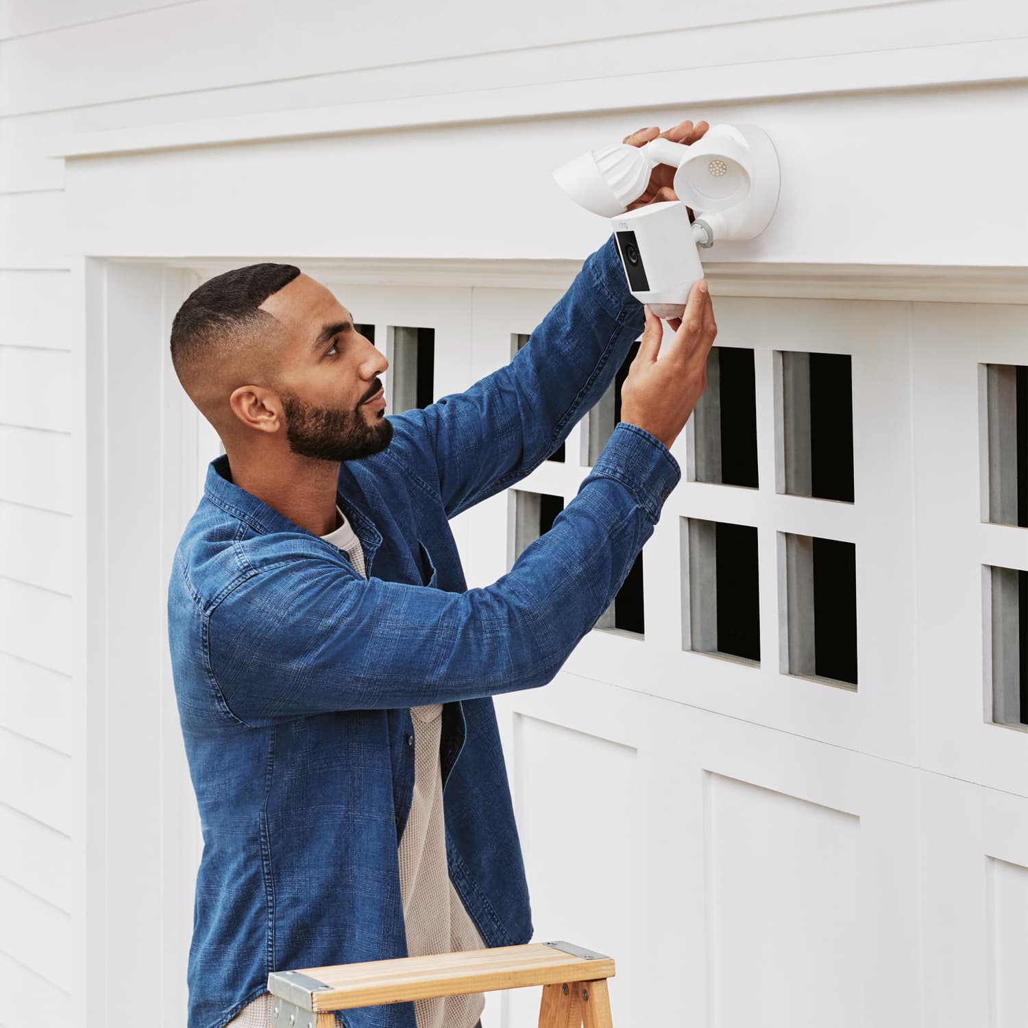 Floodlight Cam Wired Plus (Certified Refurbished) - Man adjusting the angle of camera and lights on Ring Floodlight Cam Wired Plus mounted over a garage door.