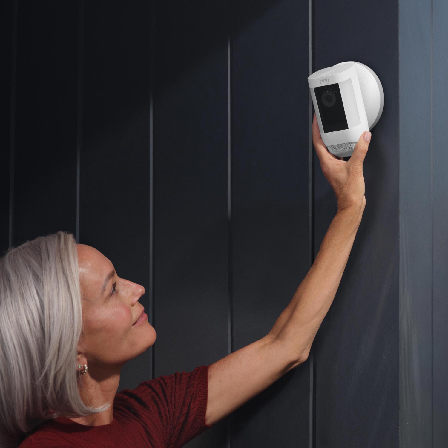 Hardwired Kit for Cameras (Outdoor Cam Plus, Spotlight Cam Plus, Spotlight Cam Pro) - Woman adjusts white Ring Spotlight Cam mounted on dark wall using the Hardwired Kit's round mounting plate.