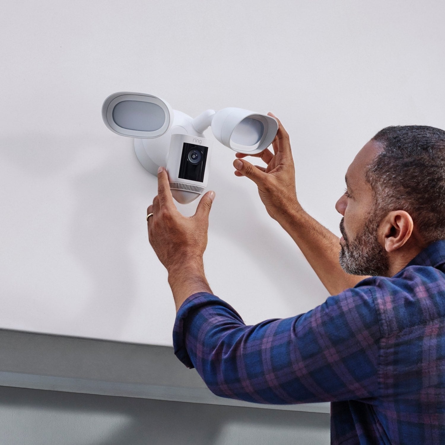 Whole-Home Starter Bundle - Person adjusting a Ring Floodlight Cam Wired Pro mounted on a wall, showing its dual lights and security camera.