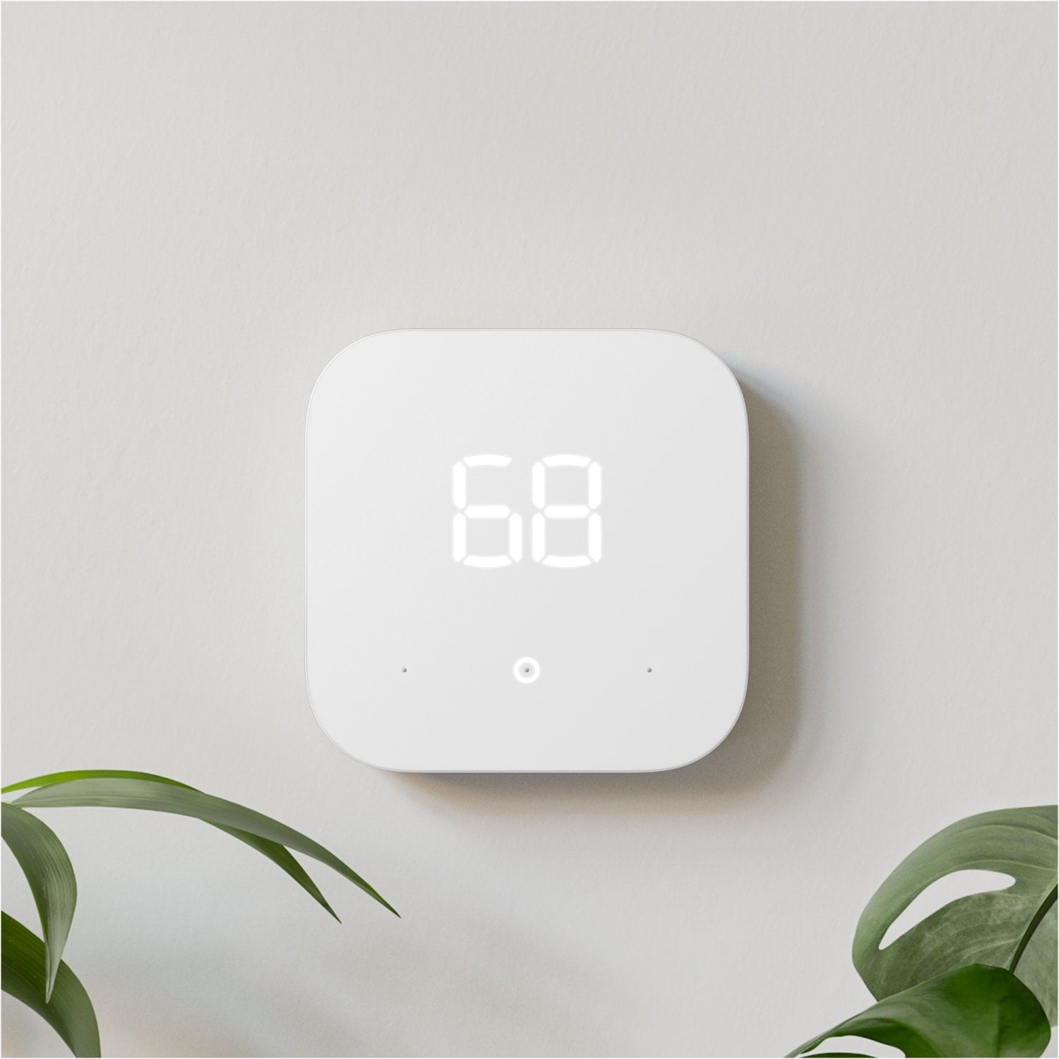 Amazon Smart Thermostat - White Amazon Smart Thermostat mounted on wall displaying 68 degrees, with green plants partially visible nearby.