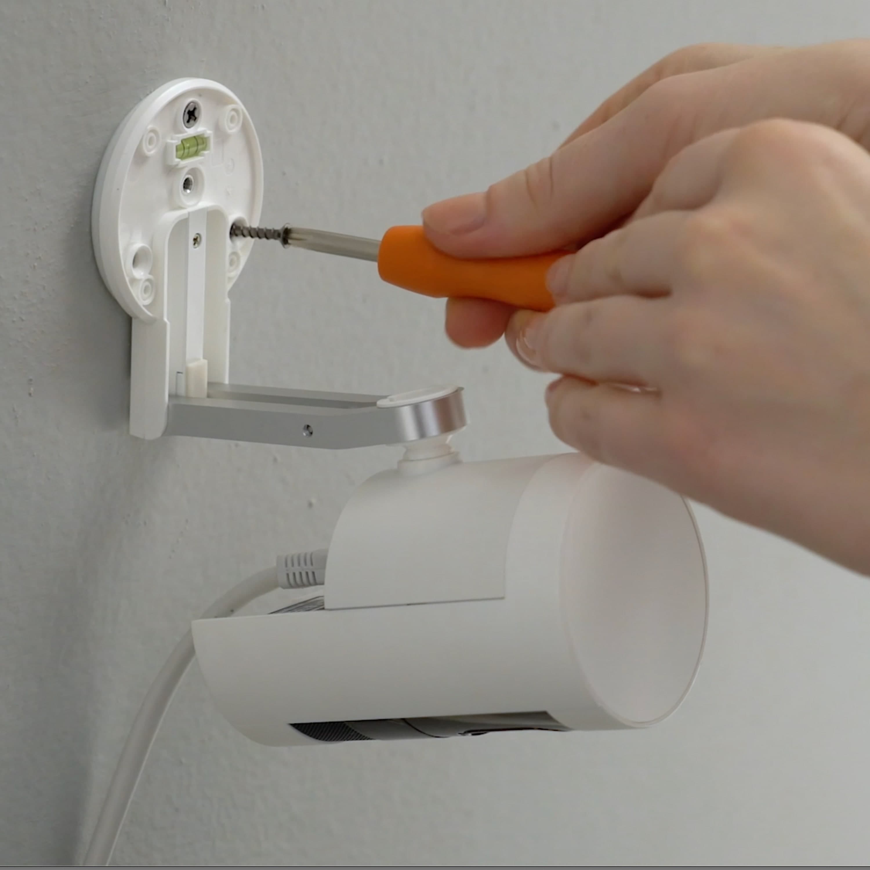 Stick Up Cam Elite with PoE Adapter - Hands use a screwdriver to mount a white Ring Stick Up Cam Elite on a wall, with visible Power over Ethernet PoE cable connected for power and network connectivity.
