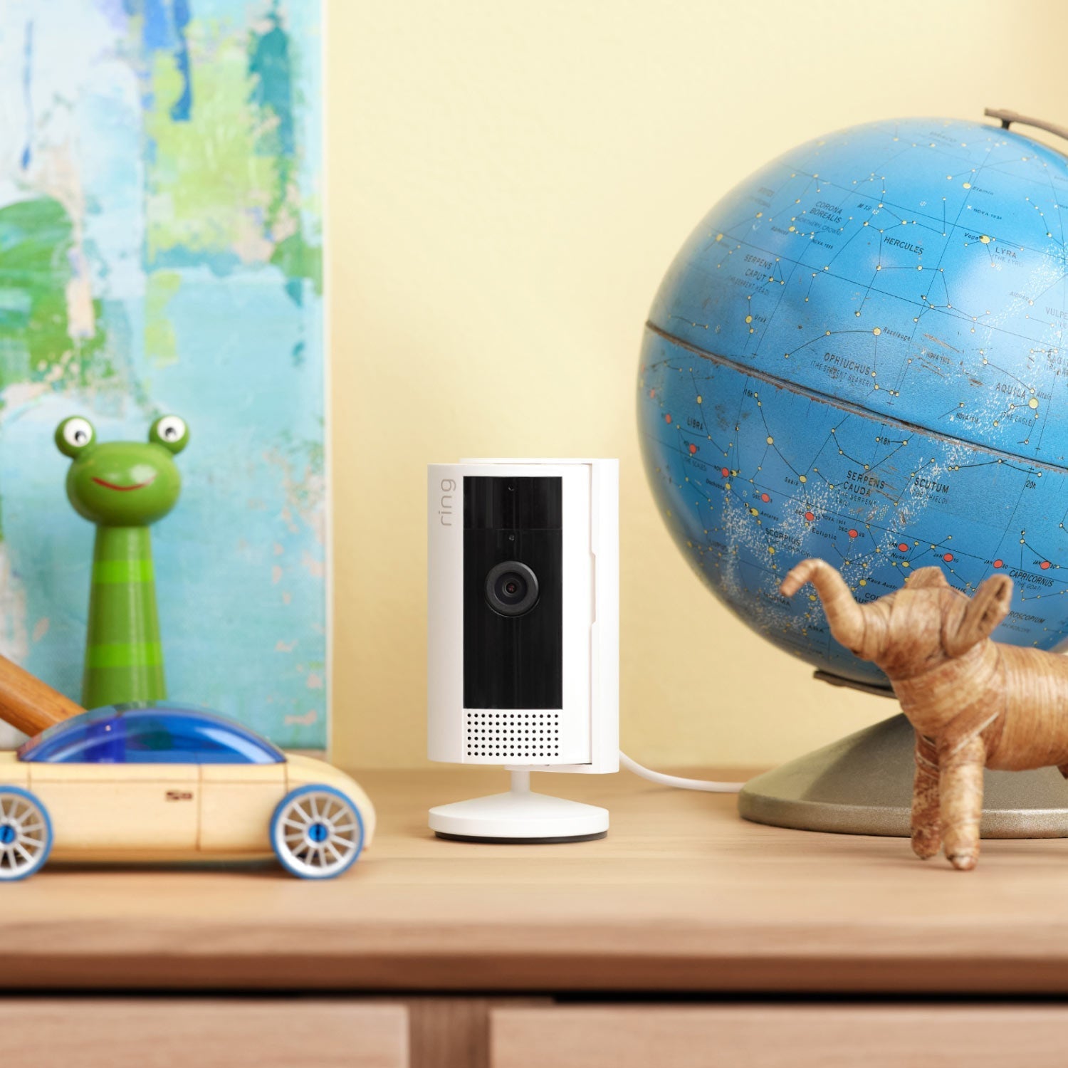 Indoor Cam, 2nd Gen (Certified Refurbished) - White Ring Indoor Cam on wooden shelf beside a toy car, a globe, and toy elephant, in brightly lit room.