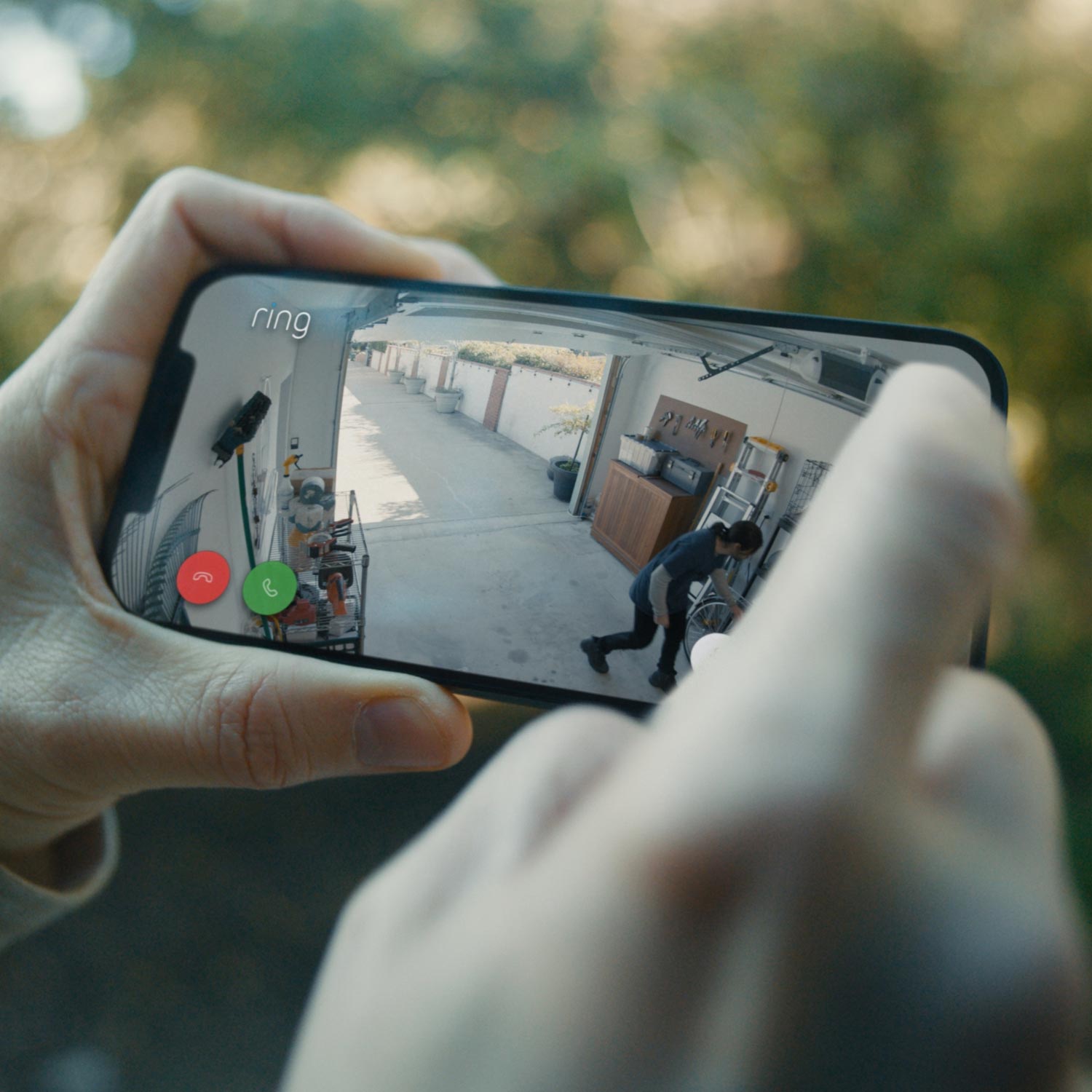 Indoor Cam, 2nd Gen (Certified Refurbished) - Person using a smartphone to view a live Ring Indoor Cam video feed of a suspicious person inside a garage.