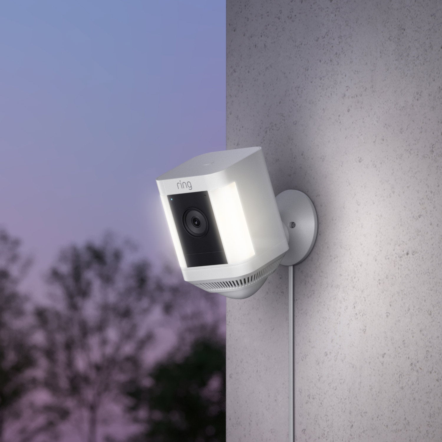 Spotlight Cam Plus - Plug-In:White Ring Spotlight Cam Plus with motion-activated lights and camera, mounted on an exterior wall at dusk.