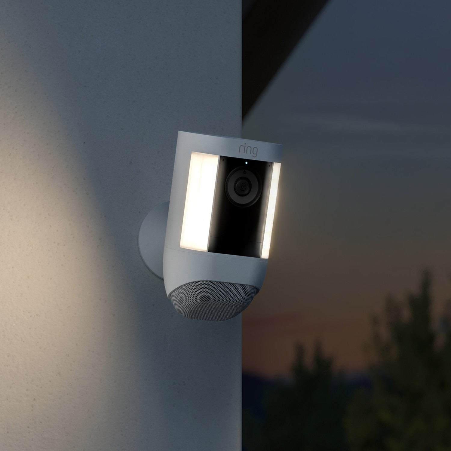 Spotlight Cam Pro (Featuring Retinal 2K) - Battery:White Ring Spotlight Cam Pro with LED lights on, mounted on an exterior wall at dusk.