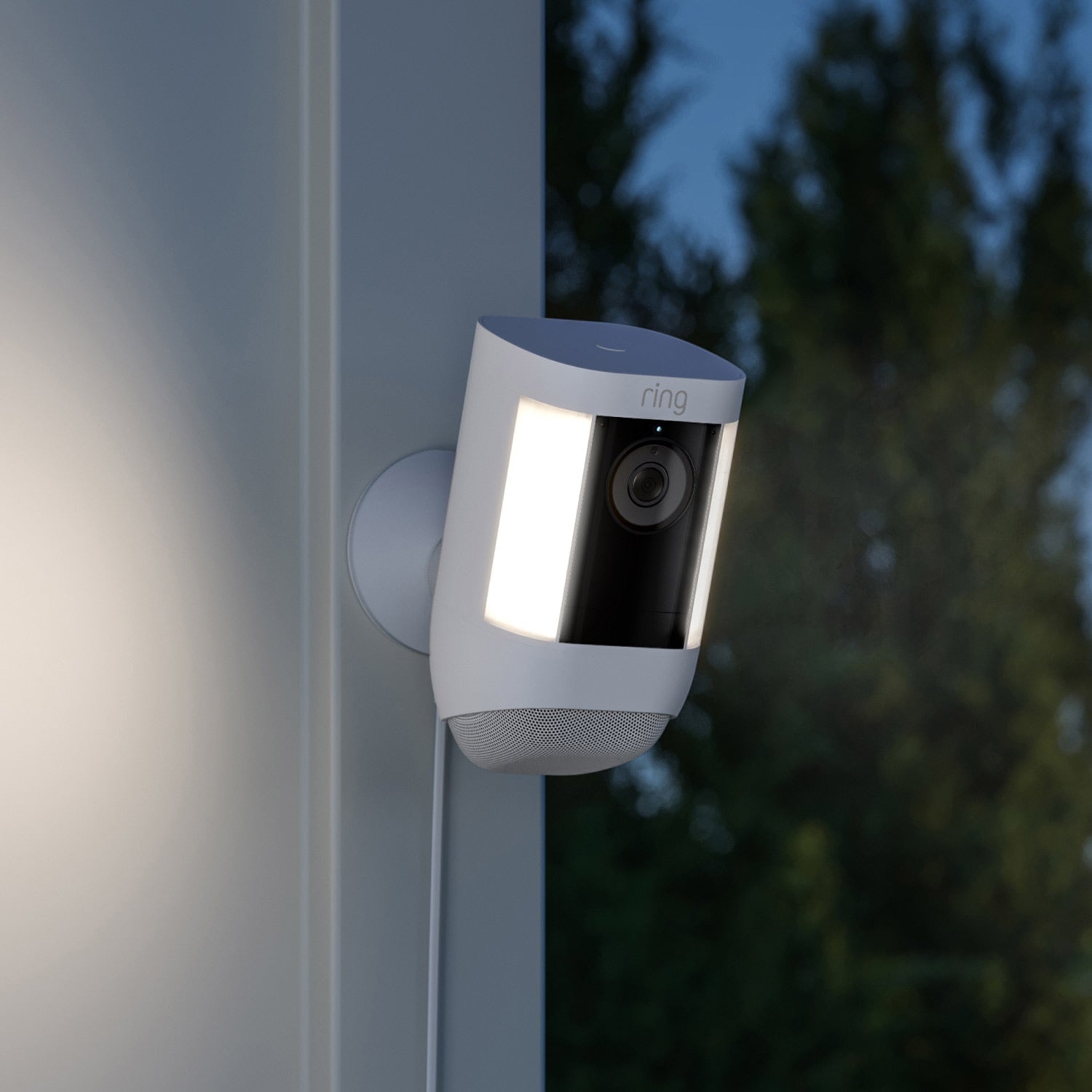Spotlight Cam Pro (Featuring Retinal 2K) - Plug-In:White Ring Spotlight Cam Pro mounted on exterior corner of home at night, lights on and connected by power cord.