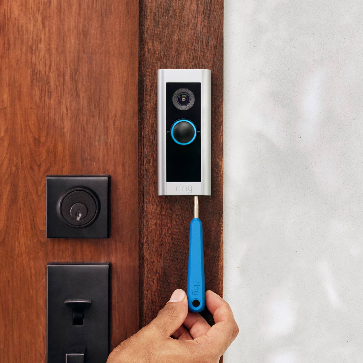 Wired Doorbell Pro (Video Doorbell Pro 2) (Certified Refurbished) - Hand using a blue Ring tool to remove or install Video Doorbell Pro 2 beside wooden front door.