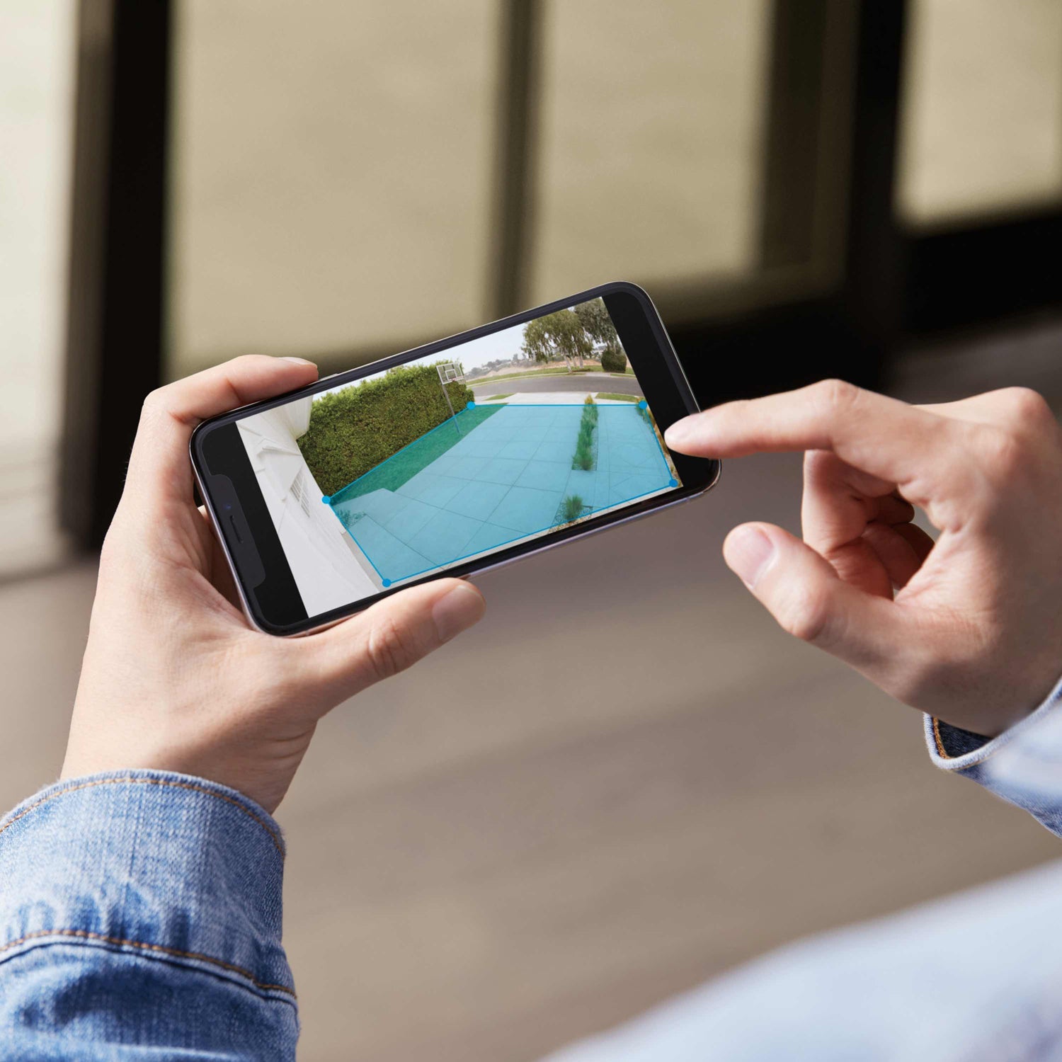 Floodlight Cam Plus - Person viewing outdoor security camera footage on smartphone, adjusting motion detection zone using the Ring App.