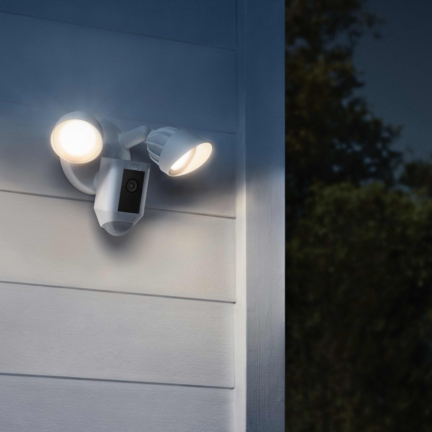 Floodlight Cam Plus - Ring Floodlight Cam Wired Plus mounted on exterior corner wall at night.