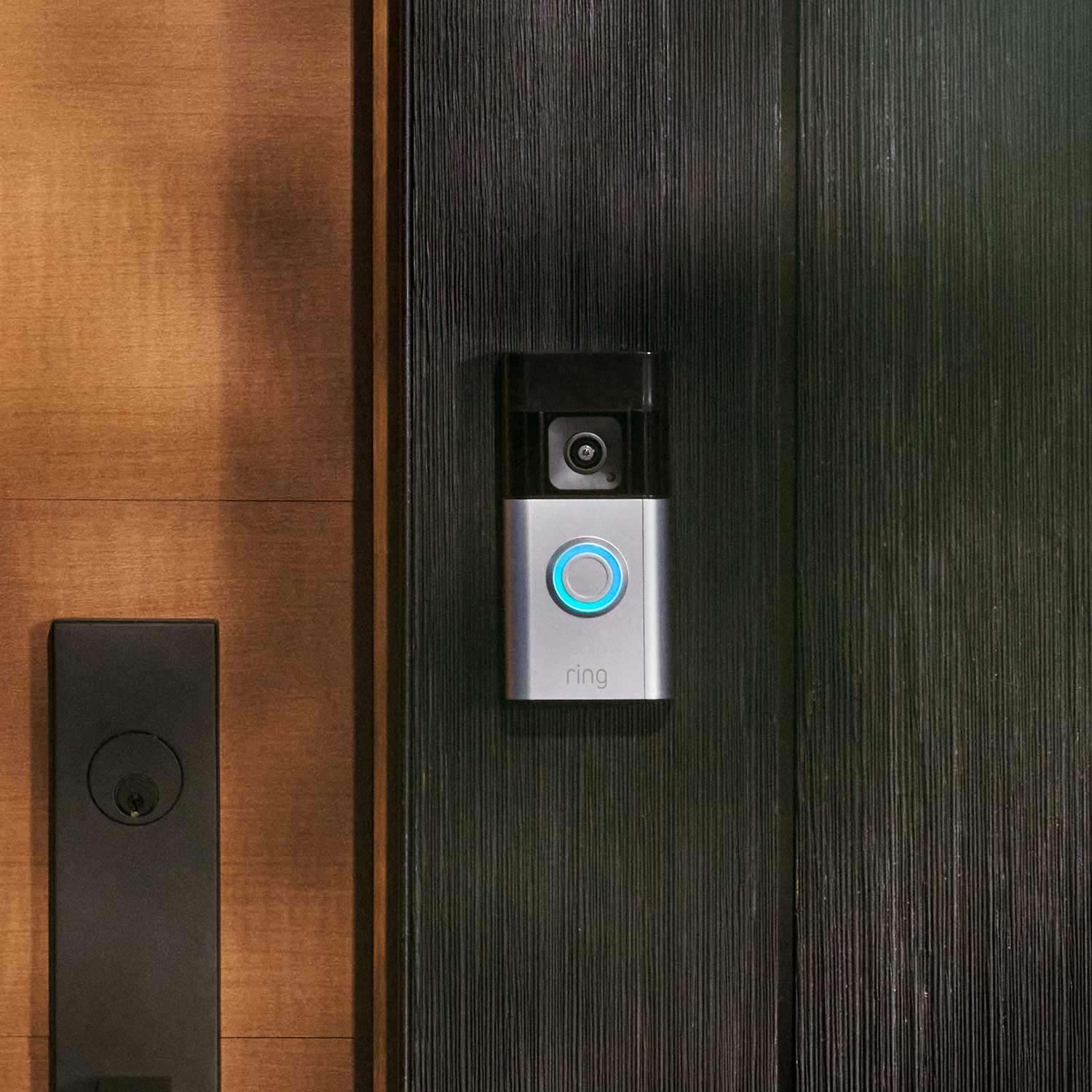 Battery Doorbell Pro + Spotlight Cam Plus Battery - Ring Battery Doorbell Pro with satin-nickel faceplate and blue-lit button beside a wooden front door.