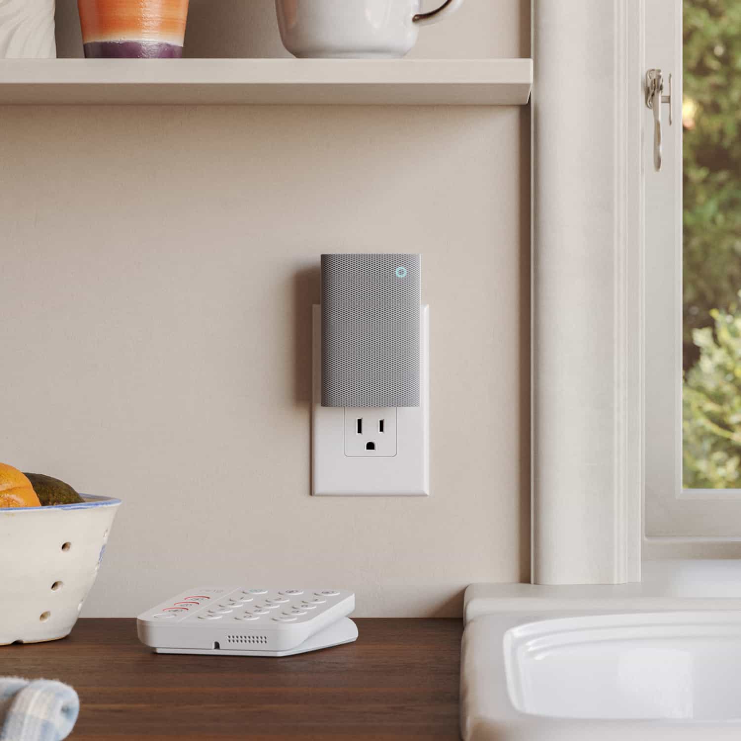 Chime Plus - Small gray smart device plugged into a kitchen outlet near a window, with a keypad on the counter and a fruit bowl on a shelf.