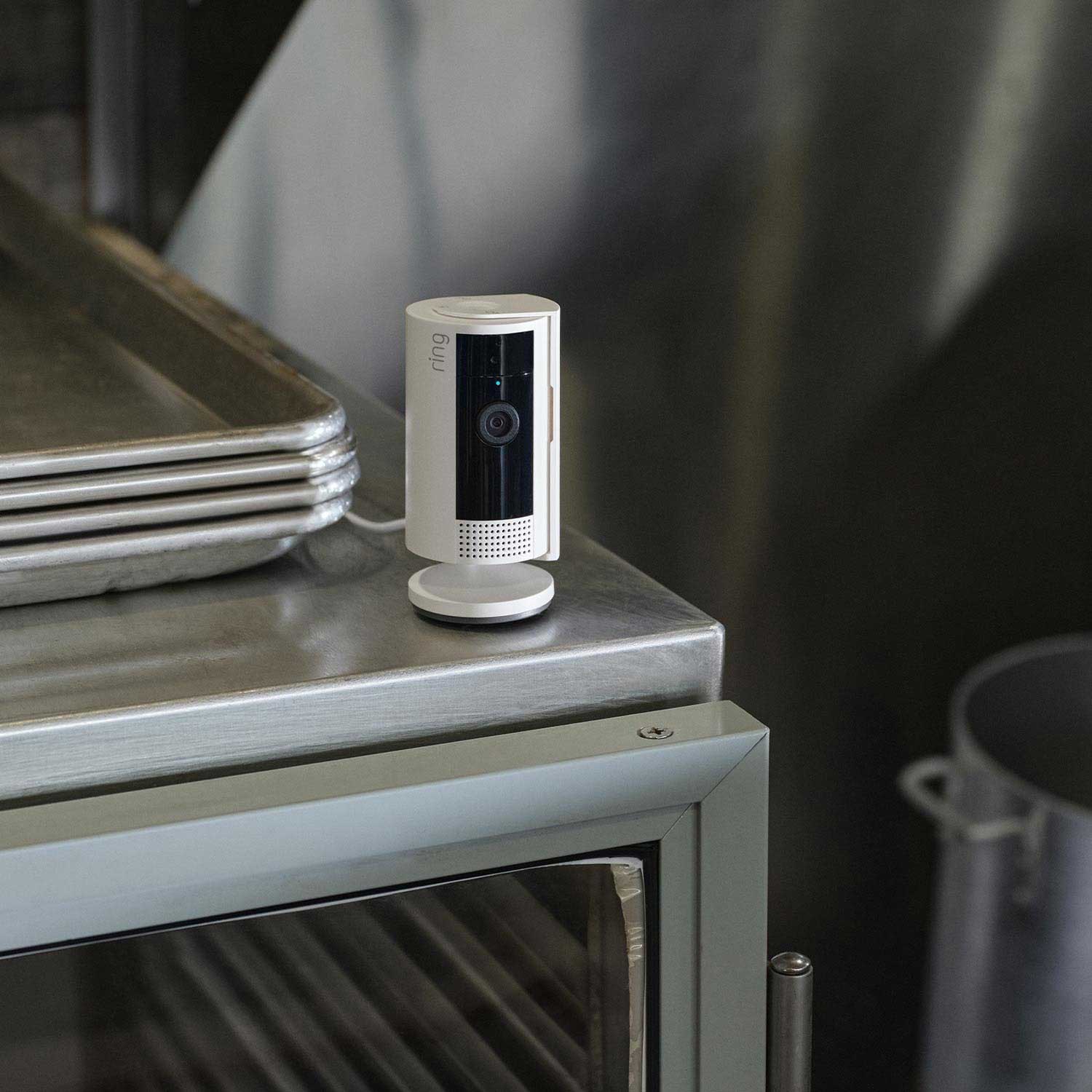Restaurant Starter Kit (Outdoor Cam Plus Battery + Indoor Cam) - A white Ring Indoor Cam standing on a metal kitchen surface next to a stack of metal baking trays.