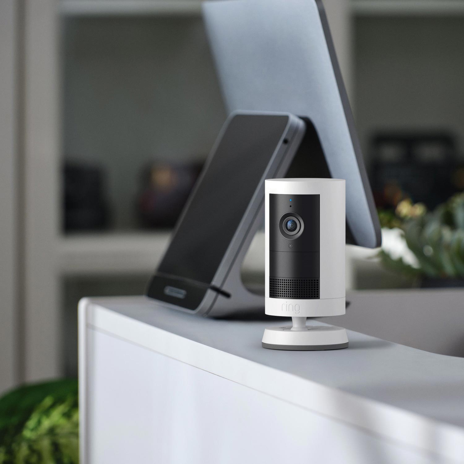 Retail Starter Kit (Plug-In) (Outdoor Cam Plus Plug-In + Pan-Tilt Indoor Cam) - White Ring security camera next to a Point of Sale system, facing the direction of customers.