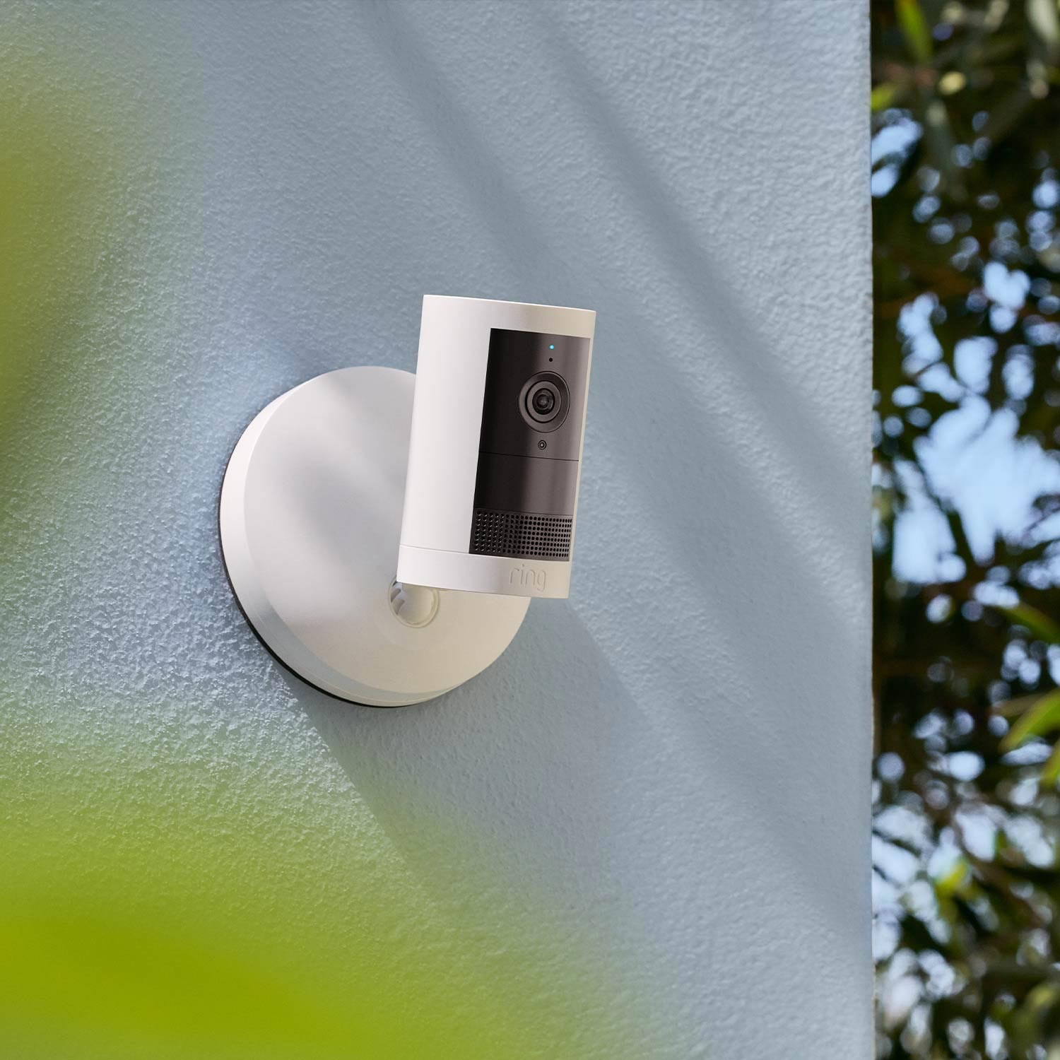 Outdoor Cam Plus (Featuring Retinal 2K)  - Wired:A White hardwired Outdoor Cam Plus mounted onto a grey stucco outdoor wall.