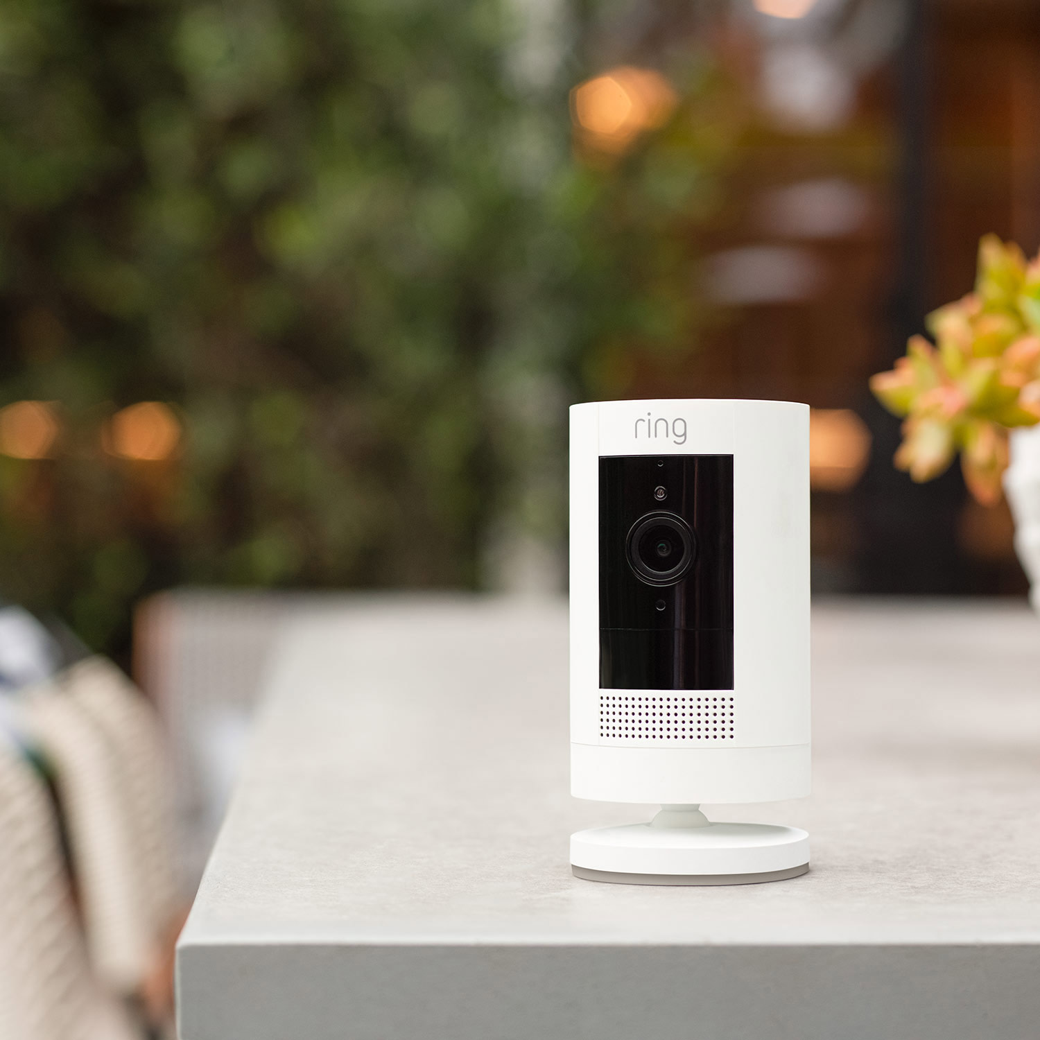 Outdoor Cam (Formerly: Stick Up Cam) - Battery:White Ring Outdoor Cam on a tabletop outdoors, showing flexible use on flat surfaces without wall mounting.