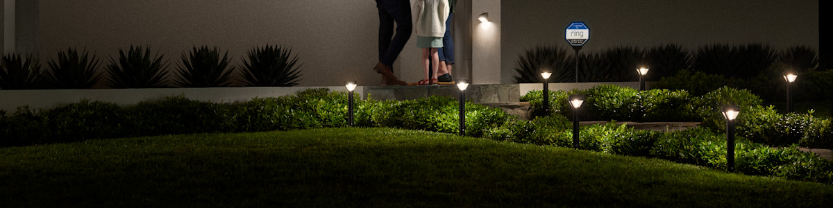 Illuminated garden path with landscape lighting with a Ring Video Doorbell and Solar Security Sign at night