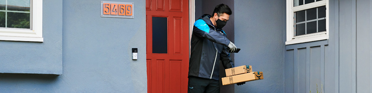 Delivery person in mask carrying Amazon packages at red door