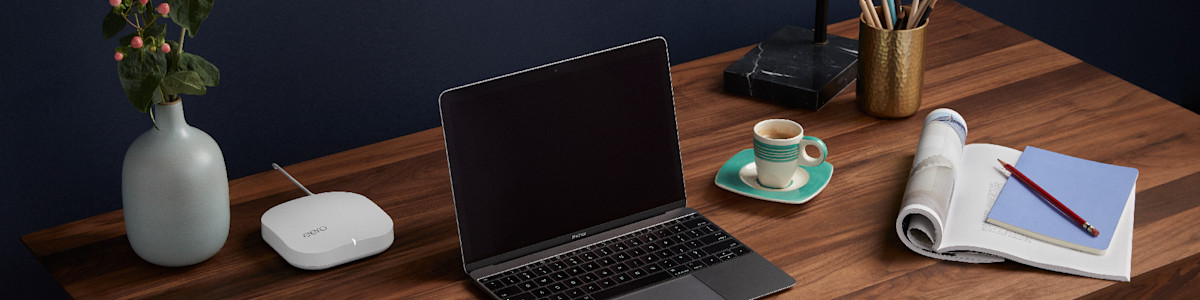 Laptop on wooden desk with coffee cup and gray vase with pink flowers